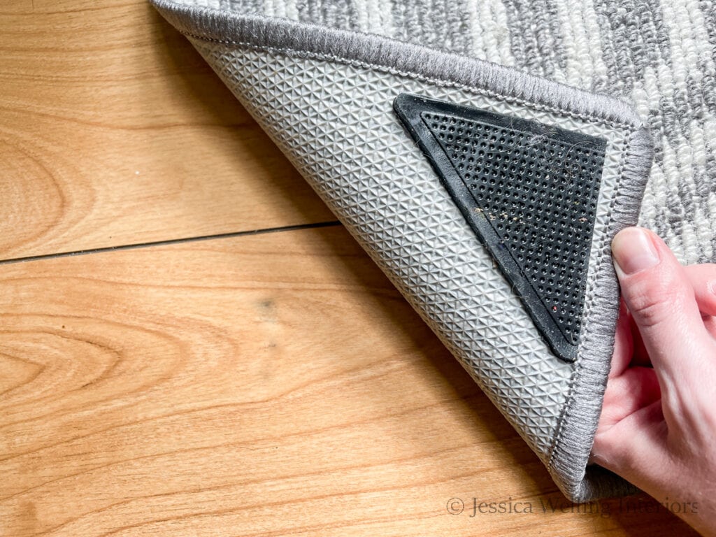 close-up of hand holding up the corner of a rug to show the rug gripper on the bottom of the rug