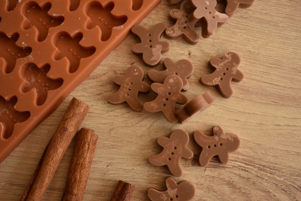 gingerbread man scented wax melts next to cinnamon sticks and a gingerbread shaped silicone mold