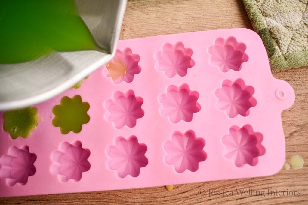 metal pitcher pouring hot wax into a flower-shaped wax melt mold