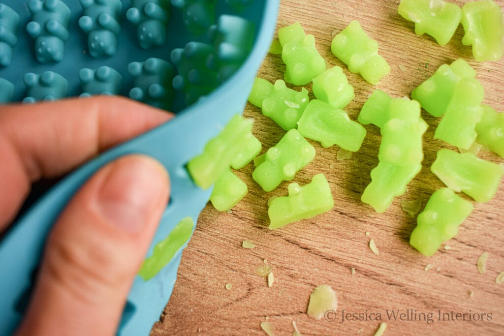 hands popping wax melts out of a gummy bear shaped mold