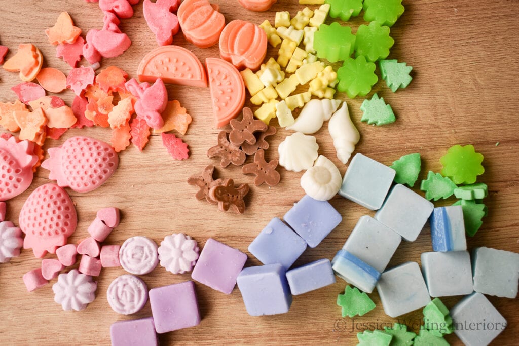 overhead view of wax melts in different sizes, shapes, and colors on a wood background