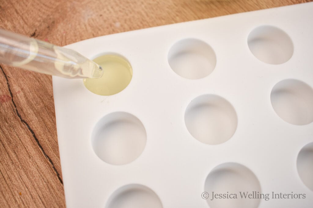 eye dropper filling the cavities of a silicone wax mold with hot wax to make wax melts