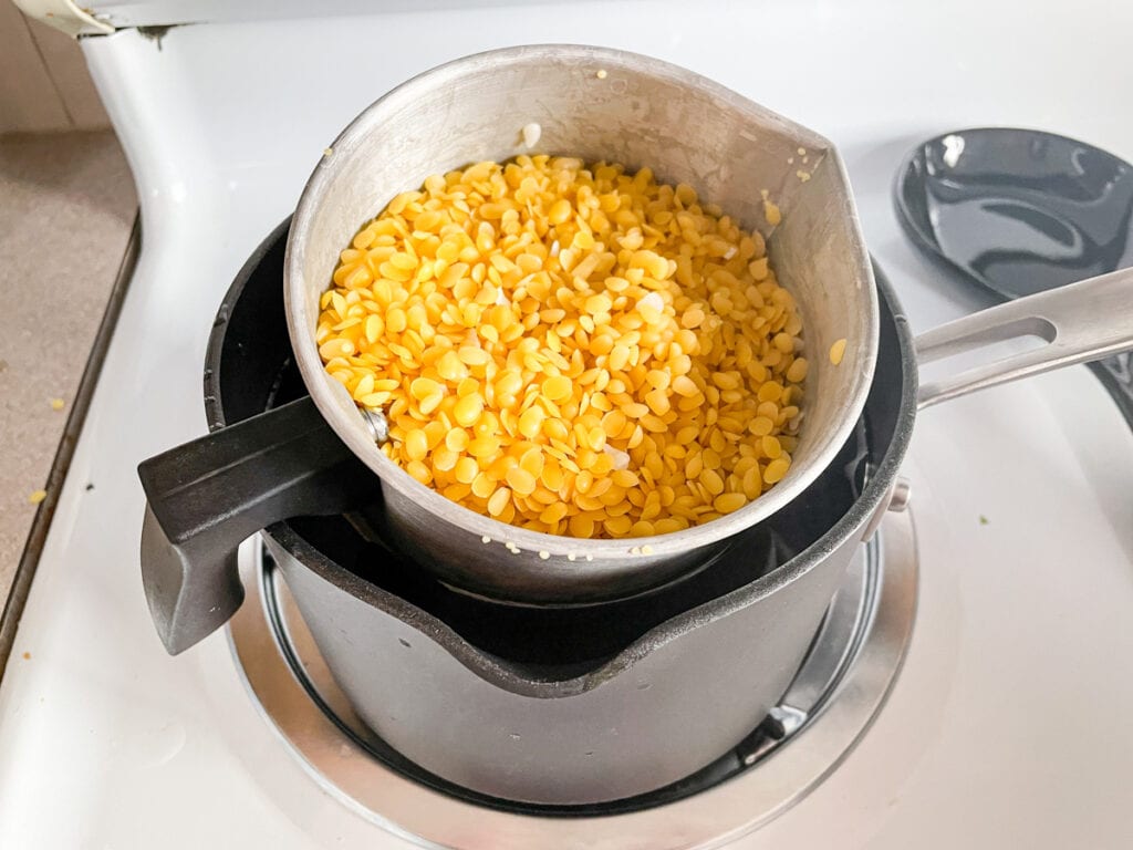 yellow beeswax pastilles melting in a double boiler over the stove