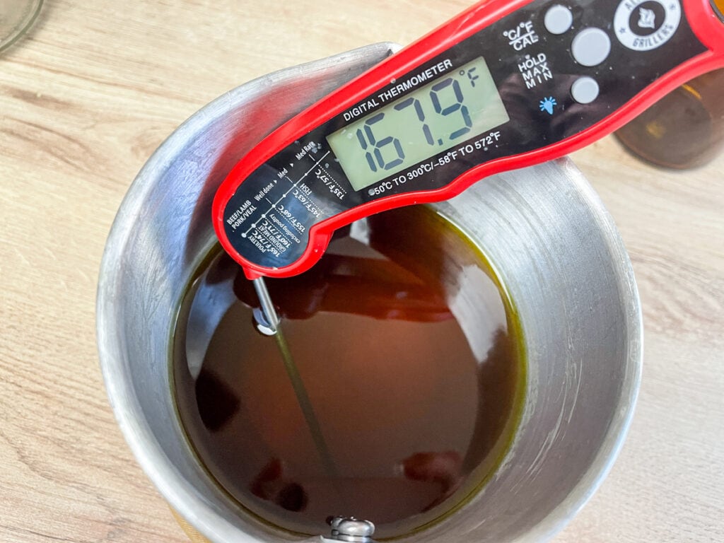 metal pitcher of melted beeswax with a digital thermometer that reads 167 degrees