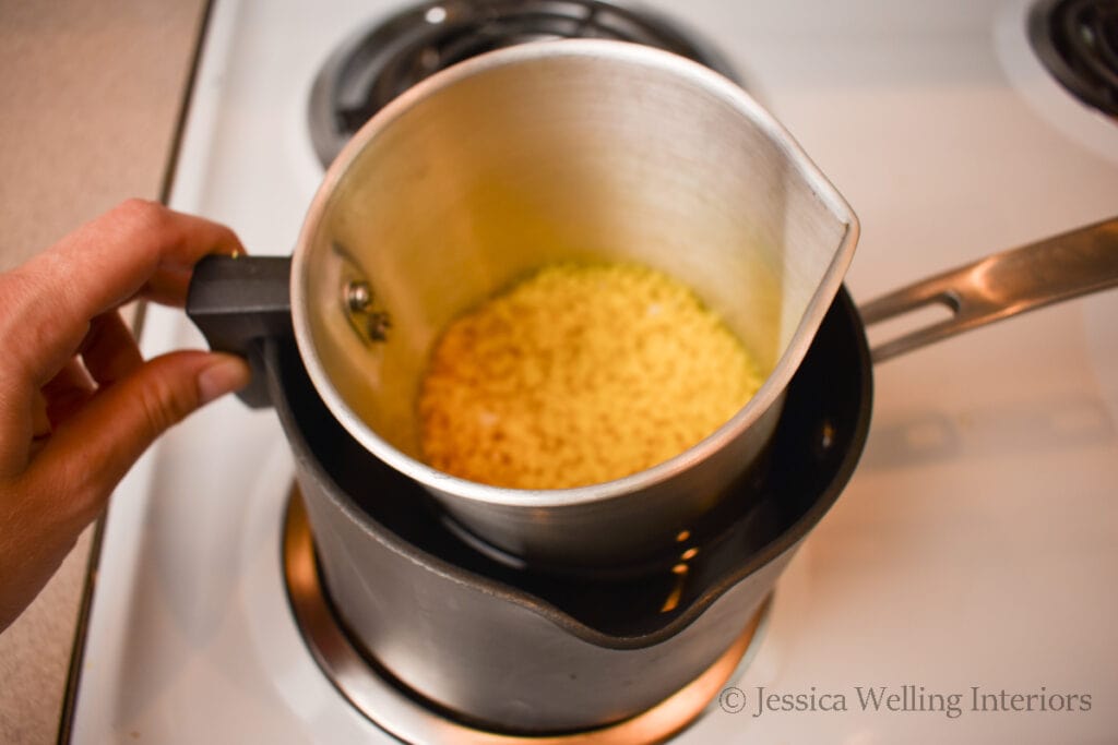 yellow beeswax pellets being melted in a double boiler on the stove top