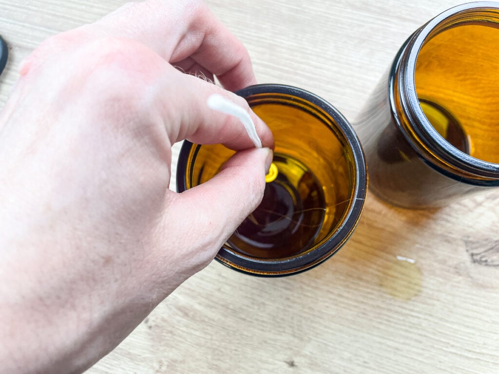 hand placing a candle wick inside an amber glass jar