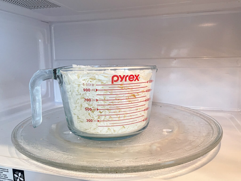 large glass measuring cup of soy wax flakes in the microwave