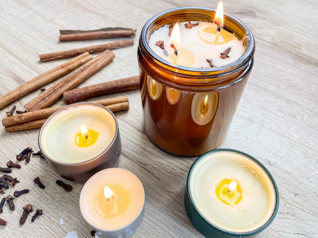 DIY scented soy candles burning with cinnamon sticks and cloves in the background