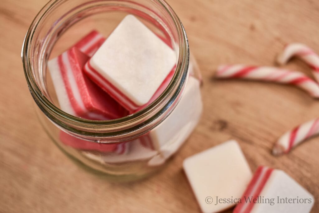 overhead view of a glass jar of red and white striped square DIY wax melts with candy canes in the background