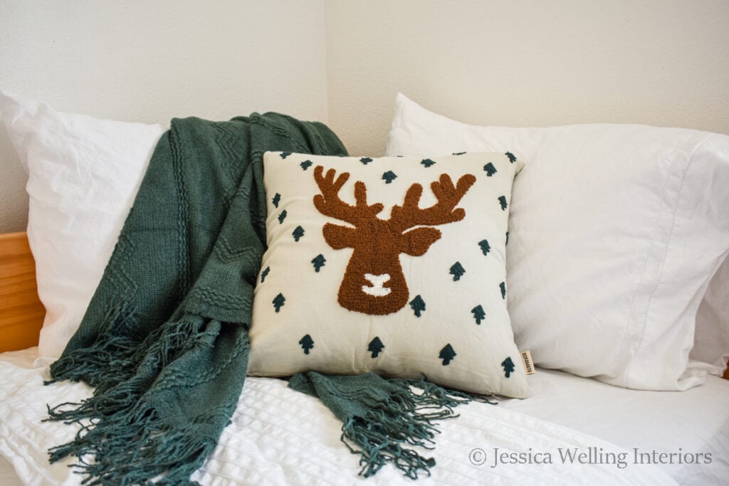cozy bed decorated for Christmas with a green Christmas blanket and reindeer pillow
