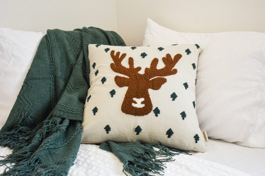 bed decorated for Christmas with a reindeer Christmas pillow cover and a green throw blanket