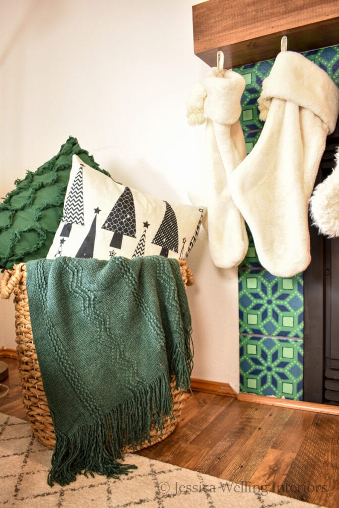 basket with Christmas throw pillows and blankets in front of a fireplace