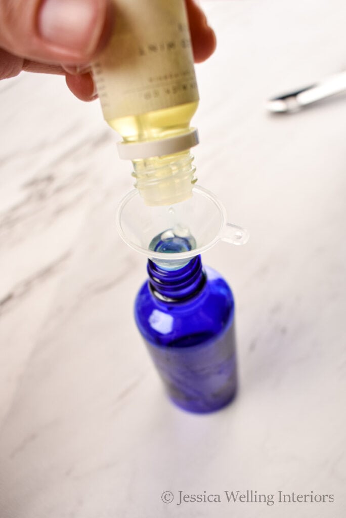 fragrance oil being poured into a blue glass spray bottle using a small funnel