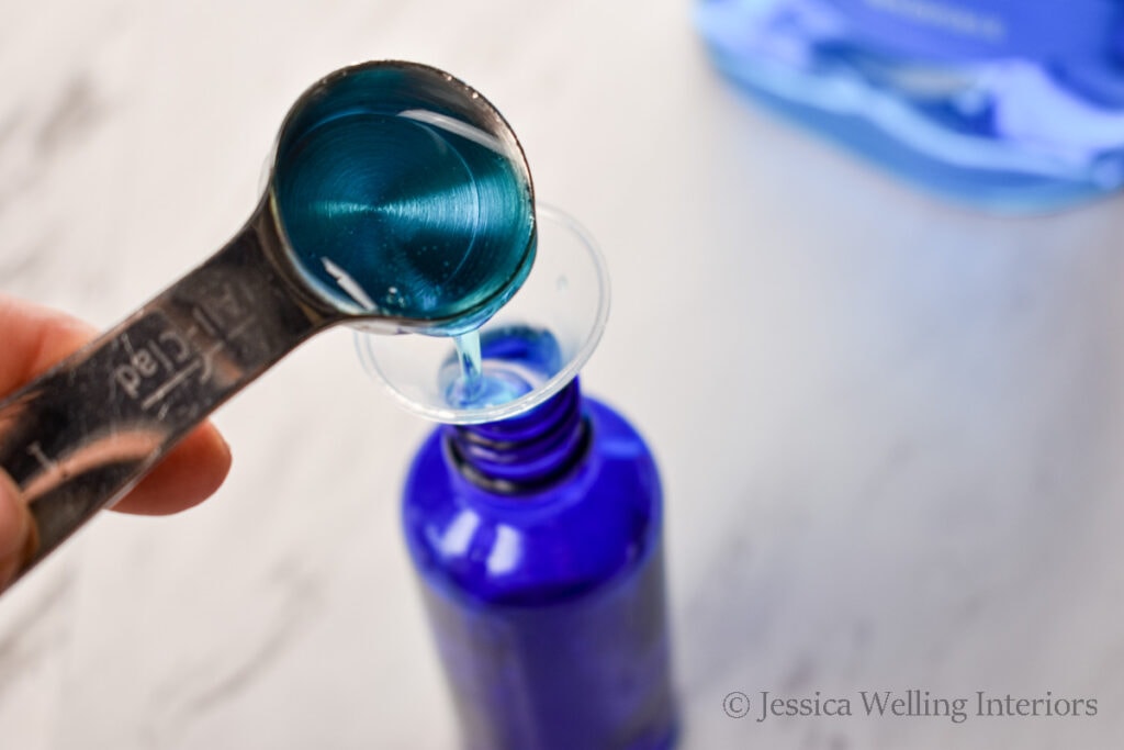 blue dish soap being poured into a funnel into a spray bottle to make Poo-pourri toilet spray