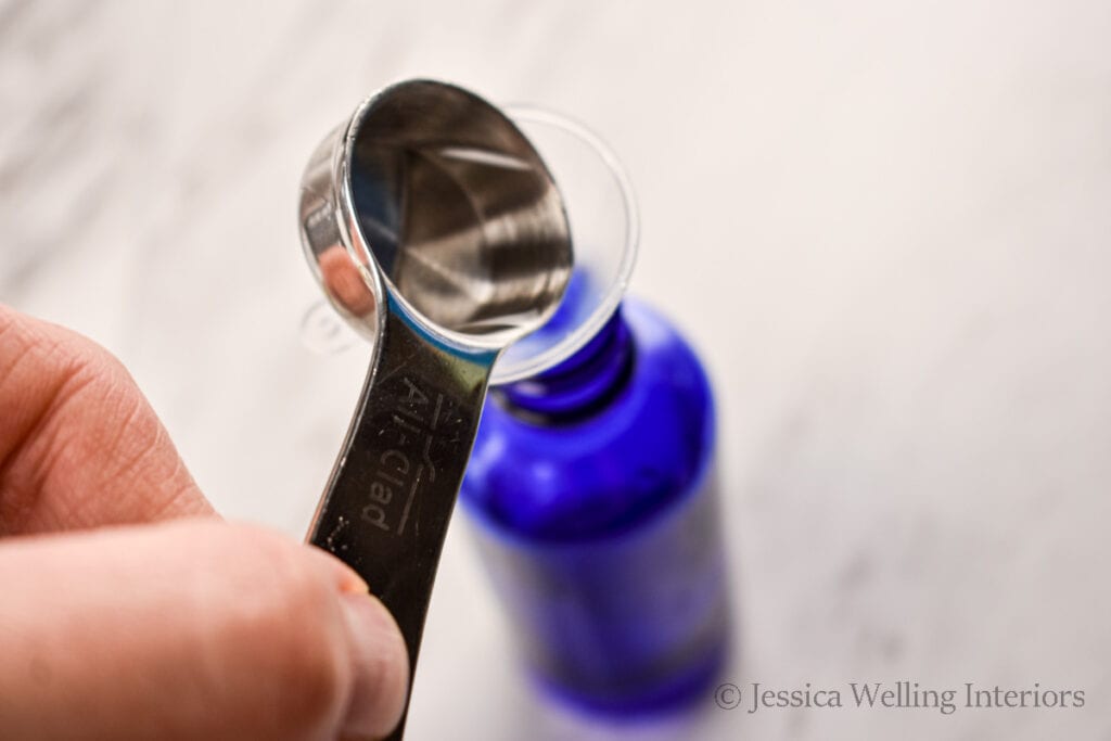 hand pouring isopropyl alcohol into the mouth of a blue glass bottle