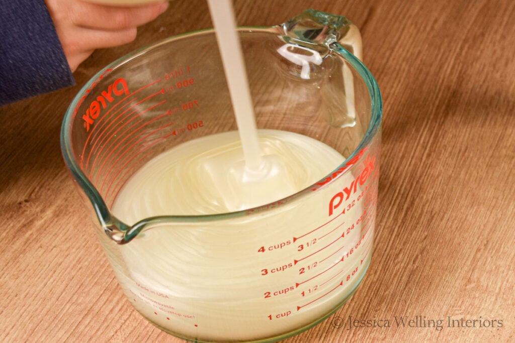 hand soap being poured into a large glass measuring cup to make DIY bubble bath