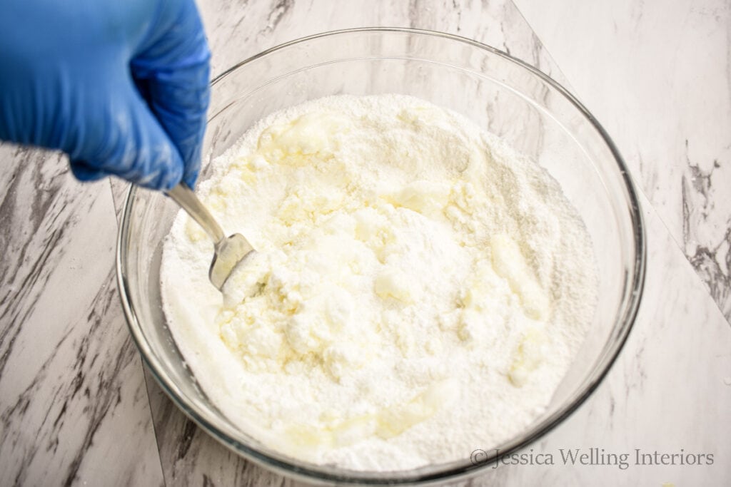 gloved hand stirring wet and dry ingredients together with a fork to make bubble bath bombs