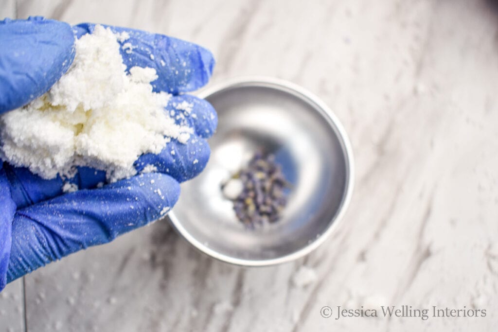 gloved hand holding bath bomb mixture over a mold