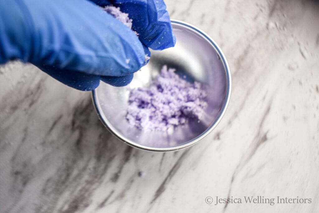 gloved hand putting purple bath bomb mixture into a mold