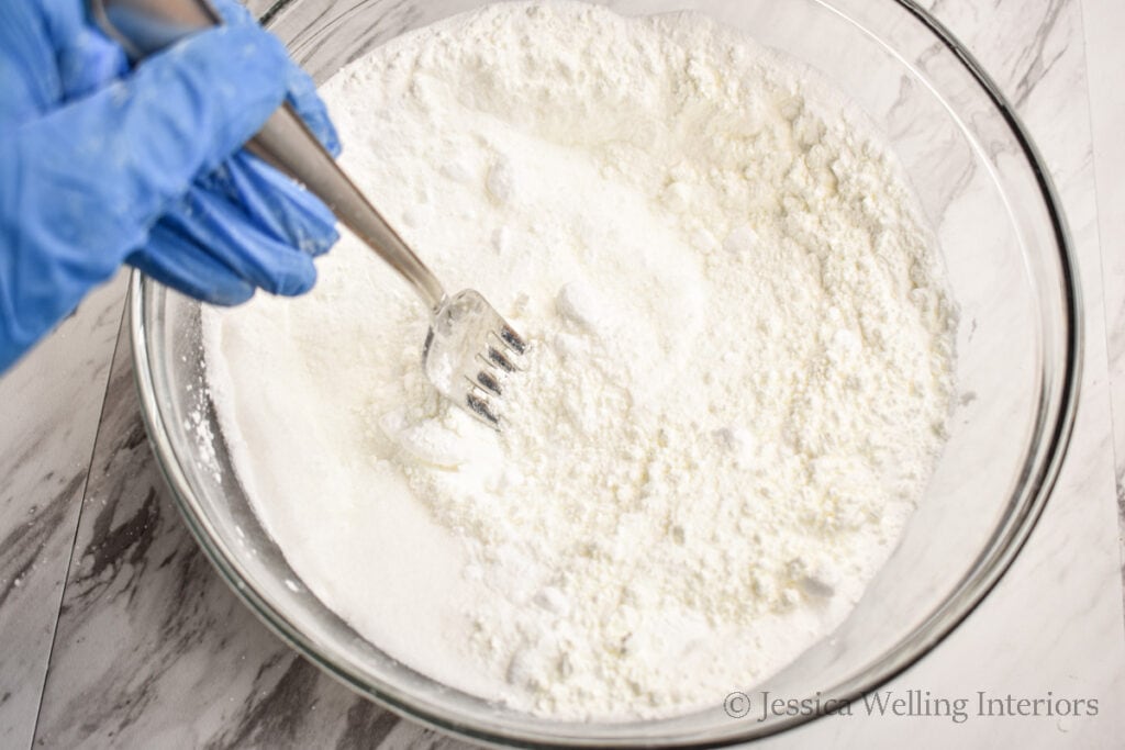 dry ingredients being combined in a bowl to make bubble bath bombs
