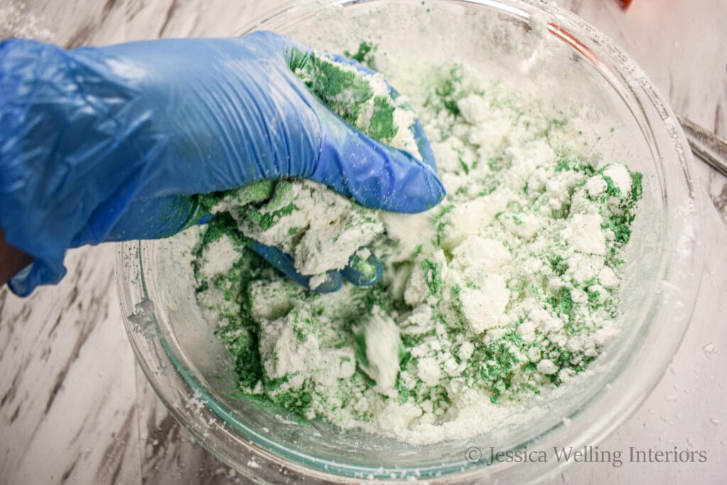 gloved hand kneading green mica powder into bath bomb mixture