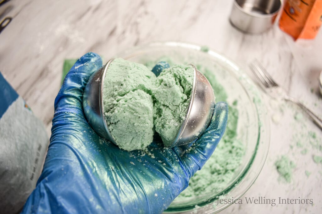 hand holding two halves of a bath bomb mold, mounded with bath bomb mixture