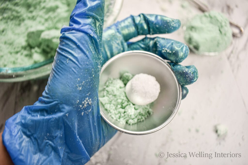 gloved hand holding a bath bomb mold with an embed in it