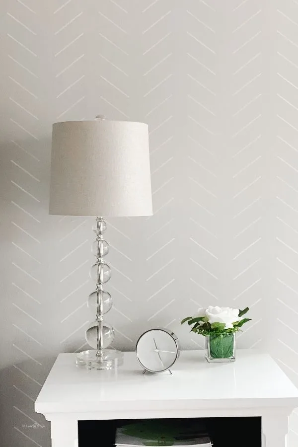 neutral stenciled accent wall with a night stand and lamp in front of it