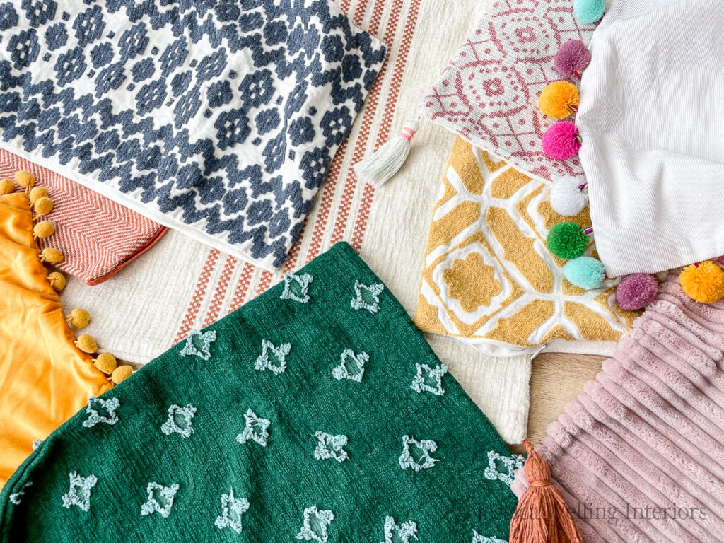 several colorful Boho pillow covers on a table with details like tassels, pom poms, embroidery, etc.