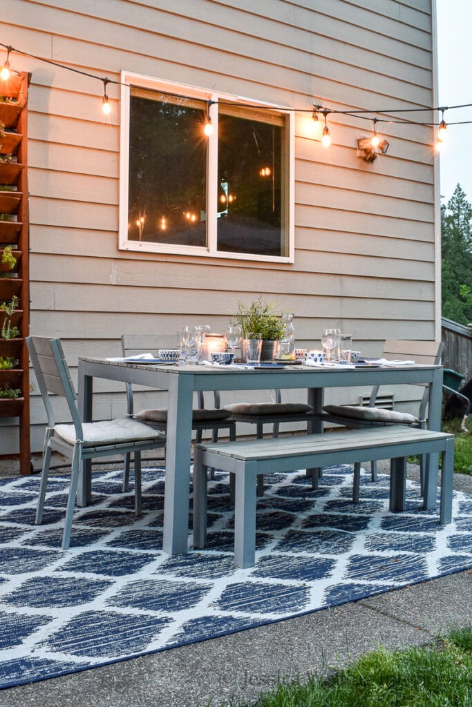 backyard patio with glowing string lights, an outdoor dining table, and a blue outdoor rug