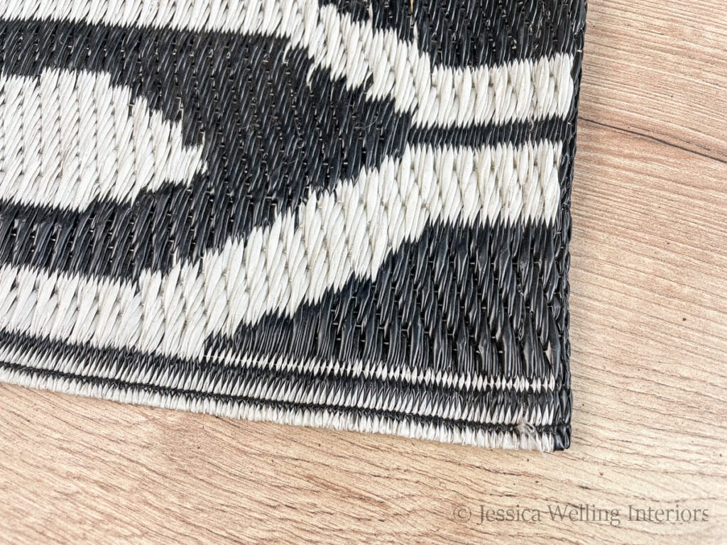 close-up of the corner of a black & white plastic outdoor rug showing it's texture and the binding on the side