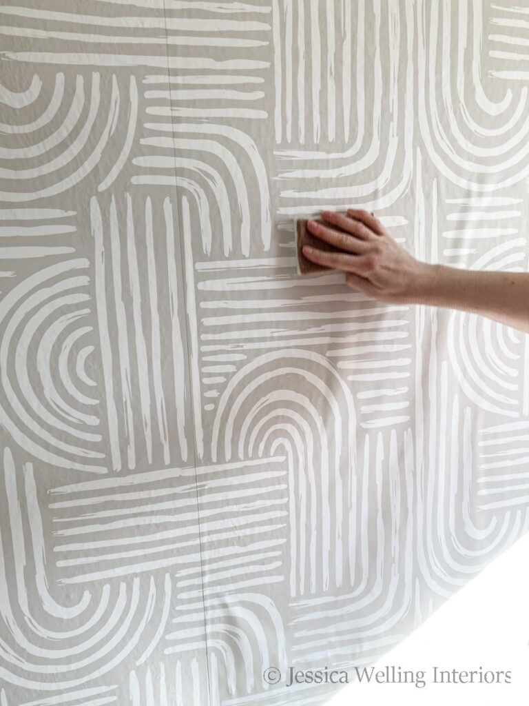hand using a wet sponge to smooth air bubbles out of wallpaper