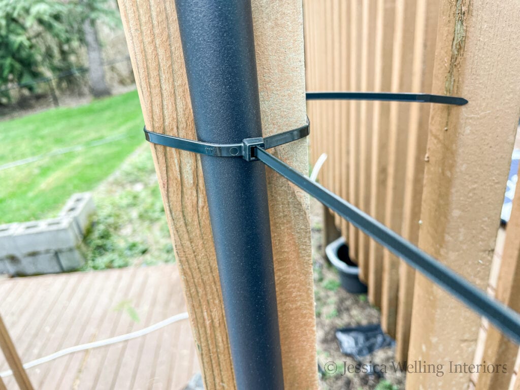 close-up of a black powder-coated string light pole attached to a deck railing post with a long zip tie