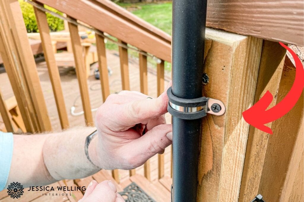 close-up of a hand holding a bracket on a string light pole and a red arrow pointing to an extra piece of wood that was added to beef up a railing post