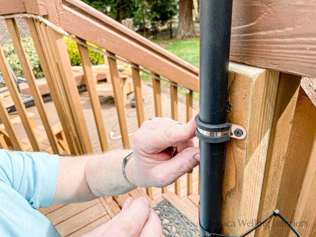 black pole being fastened to a deck post with a bracket to hang outdoor string lights