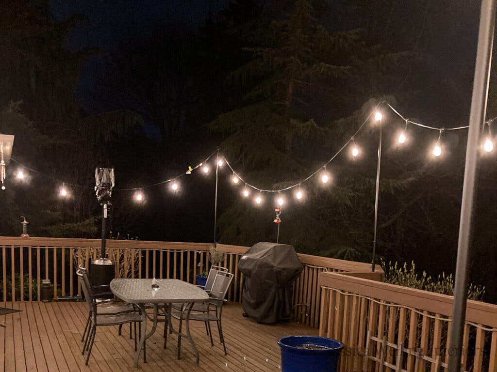 nighttime photo of glowing string lights hanging from poles attached to a deck railing