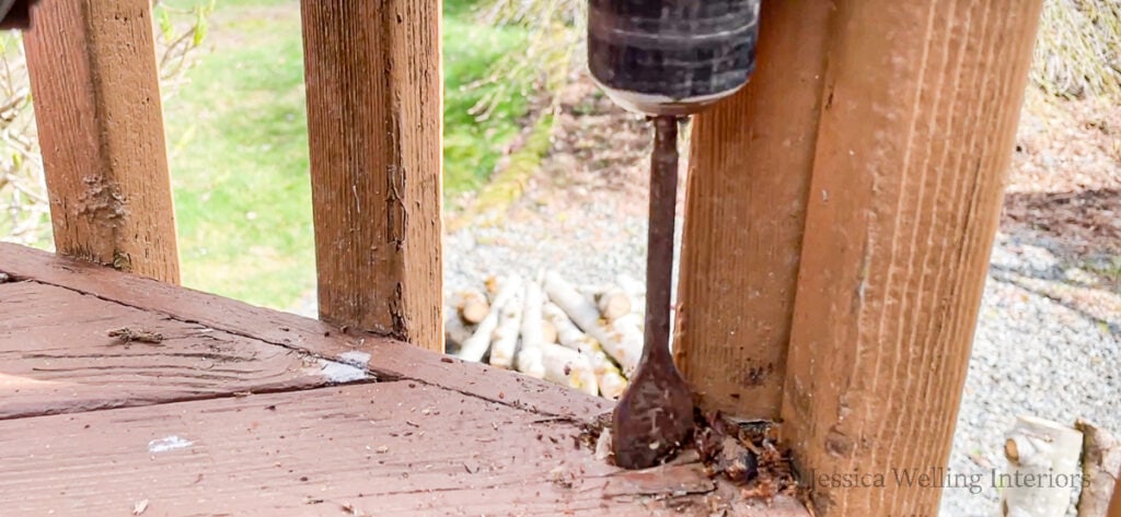 hole being drilled in the surface of a deck using an electric drill and paddle bit