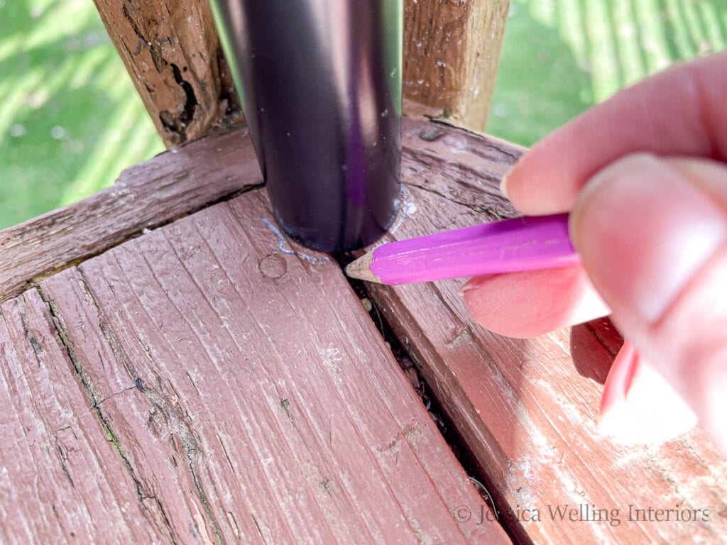 close-up of a hand using a pencil to trace the bottom of a string light pole on the surface of a deck