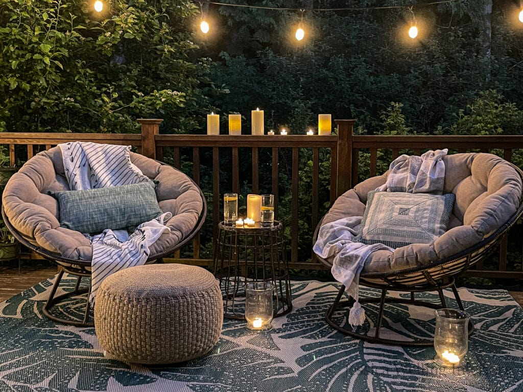 outdoor conversation set for two set up on a deck with an outdoor rug, string lights, and an outdoor pouf