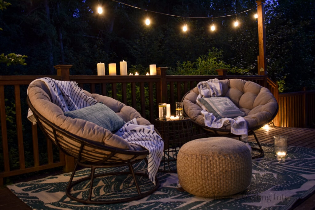 cozy Boho deck set up with papasan chairs, pillows and blankets, an outdoor rug, and glowing string lights