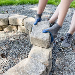 hands stacking concrete blocks to build a DIY fire pit