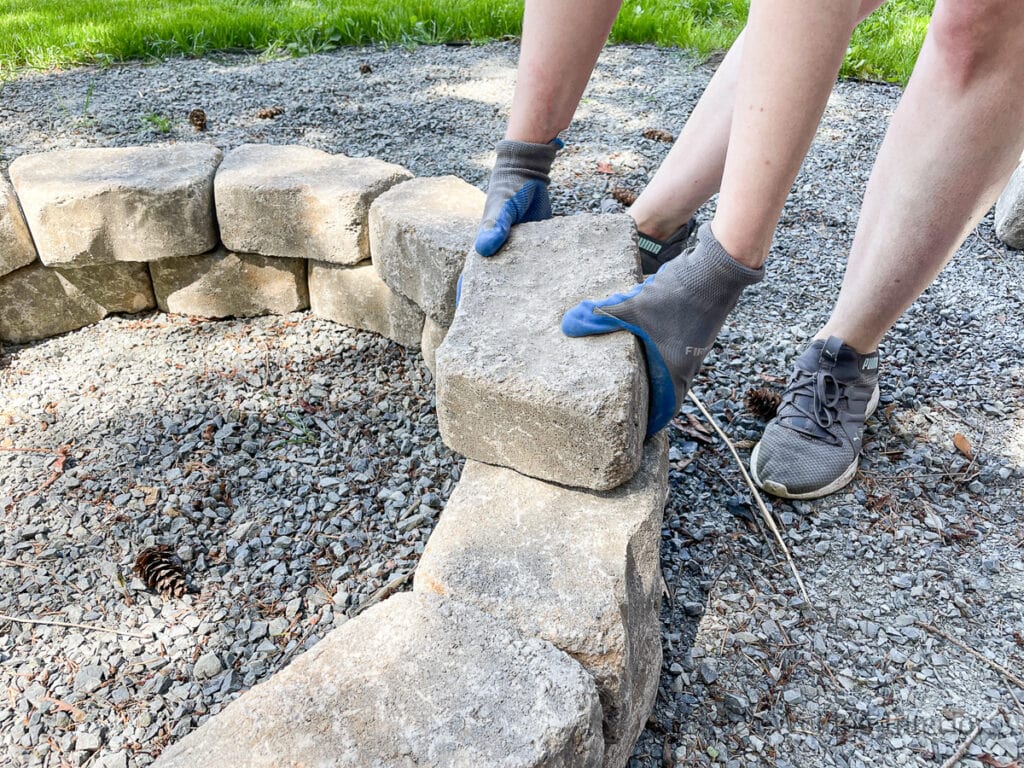 woman using gloved hands to place a concrete block on a DIY firepit