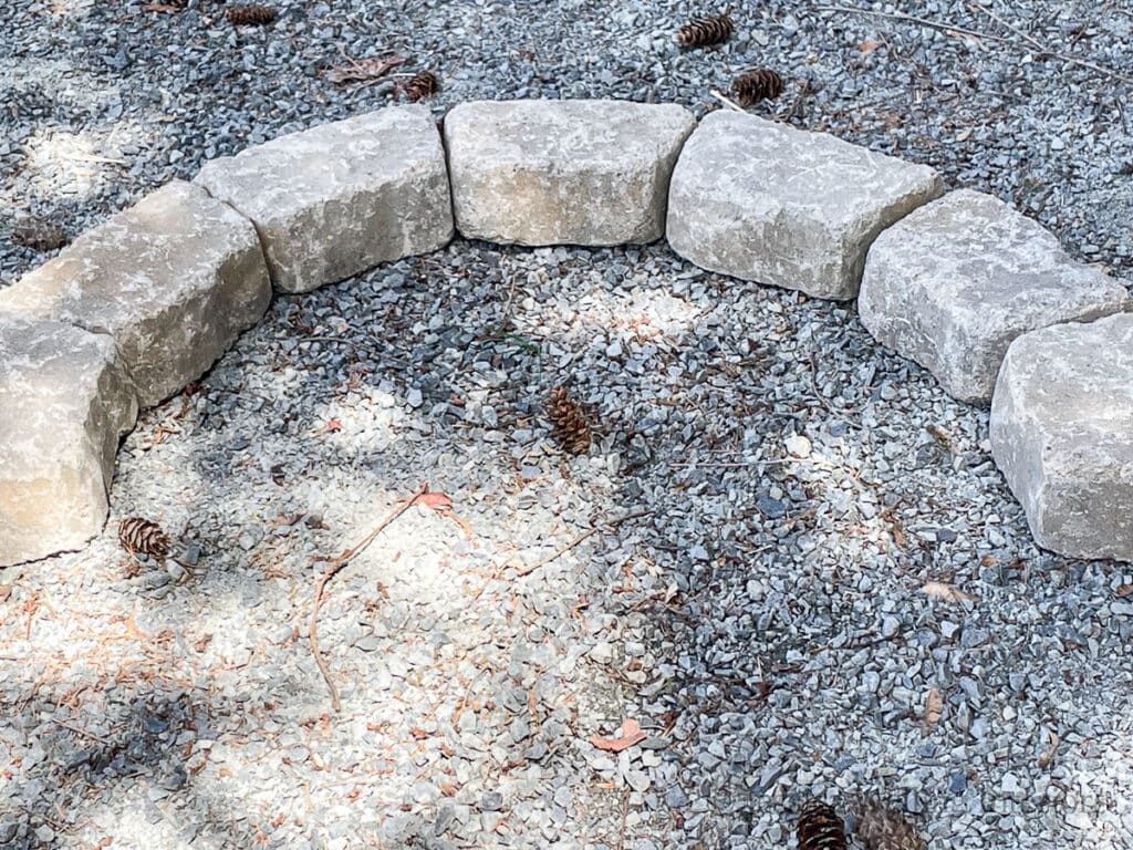 retaining wall blocks arranged in a half circle to form the first layer for a DIY backyard firepit