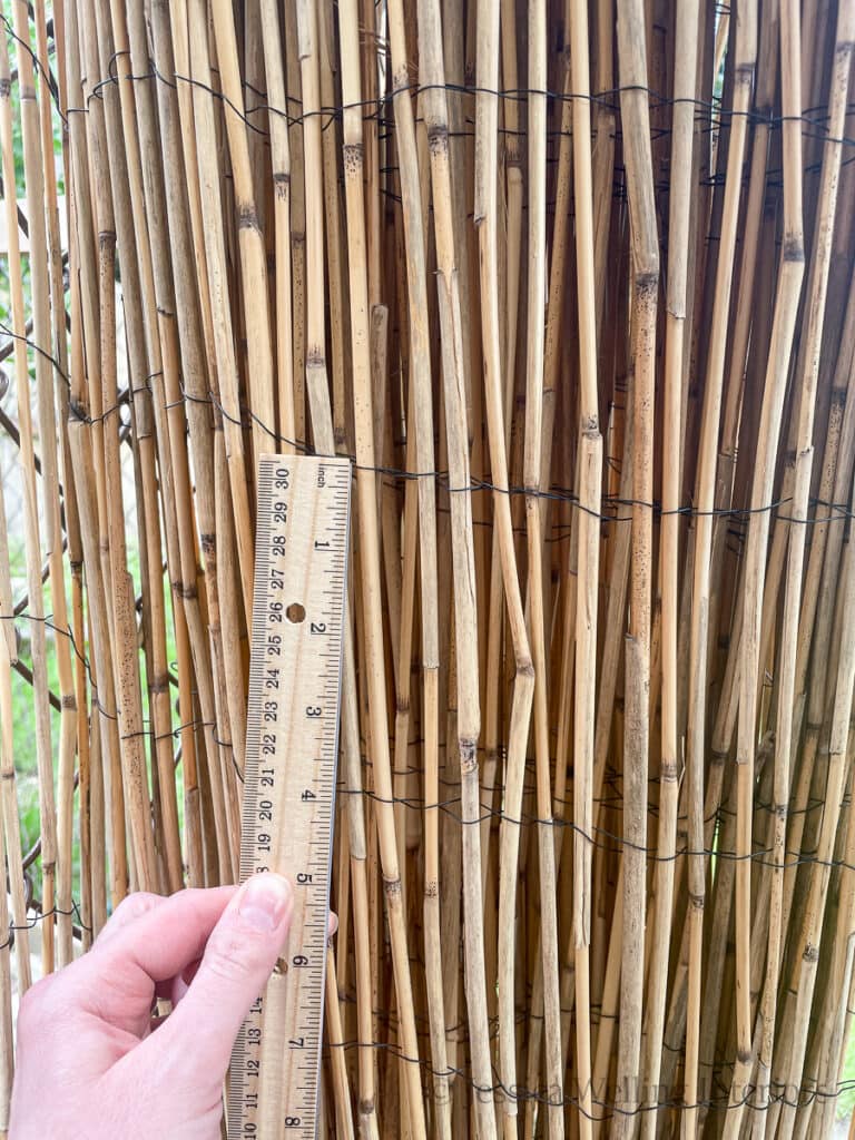close-up of wires holding bamboo privacy screening together and a hand holding a ruler in front of it