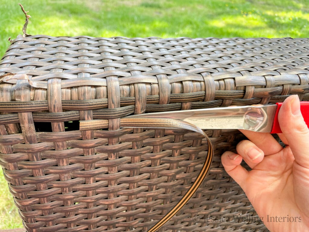 hand using a metal wicker repair tool to weave a replacement reed into a wicker sofa