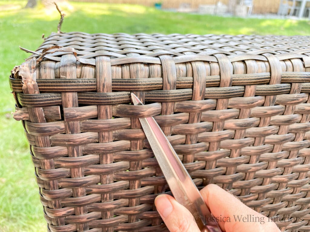 hand using a metal weaving tool to pull a damaged wicker reed out of an outdoor sofa