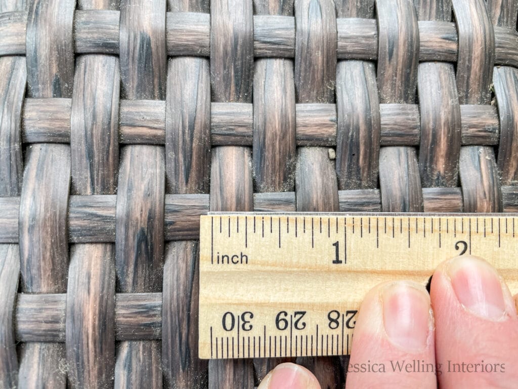 hand holding a ruler up to the wicker reeds on an outdoor sofa