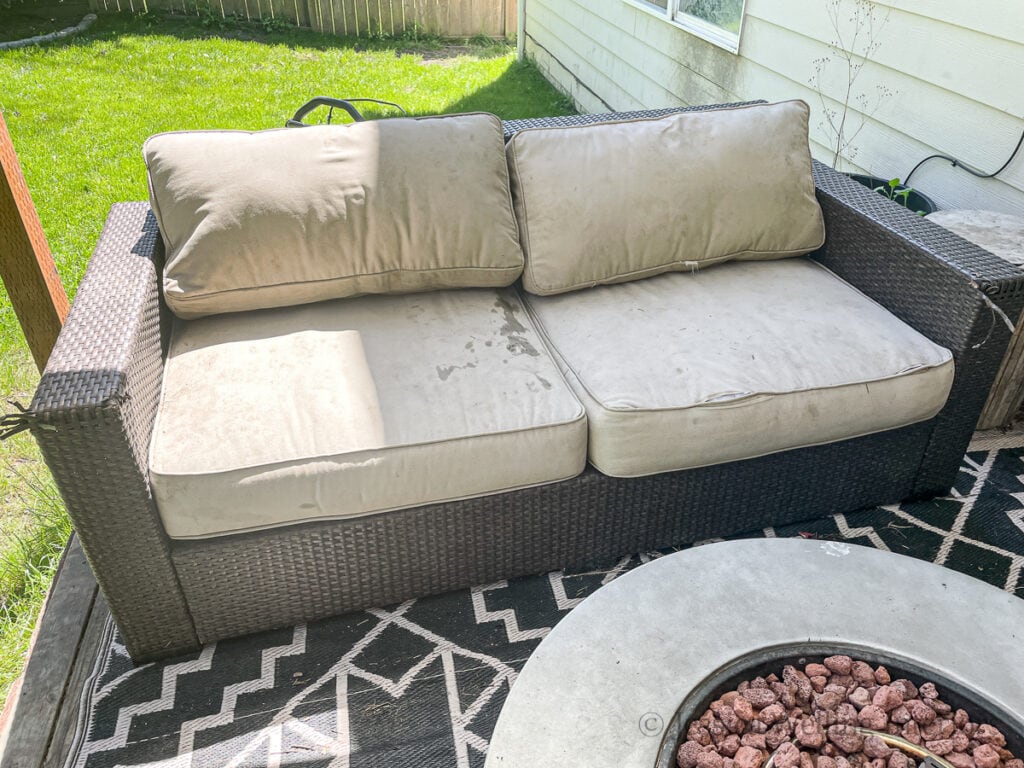 old resin wicker outdoor sofa with stained cushions and damaged wicker