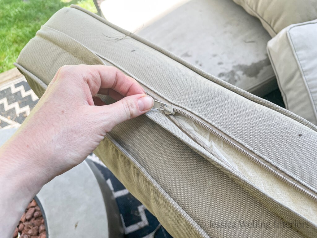 hand unzipping the cover from a patio sofa outdoor cushion