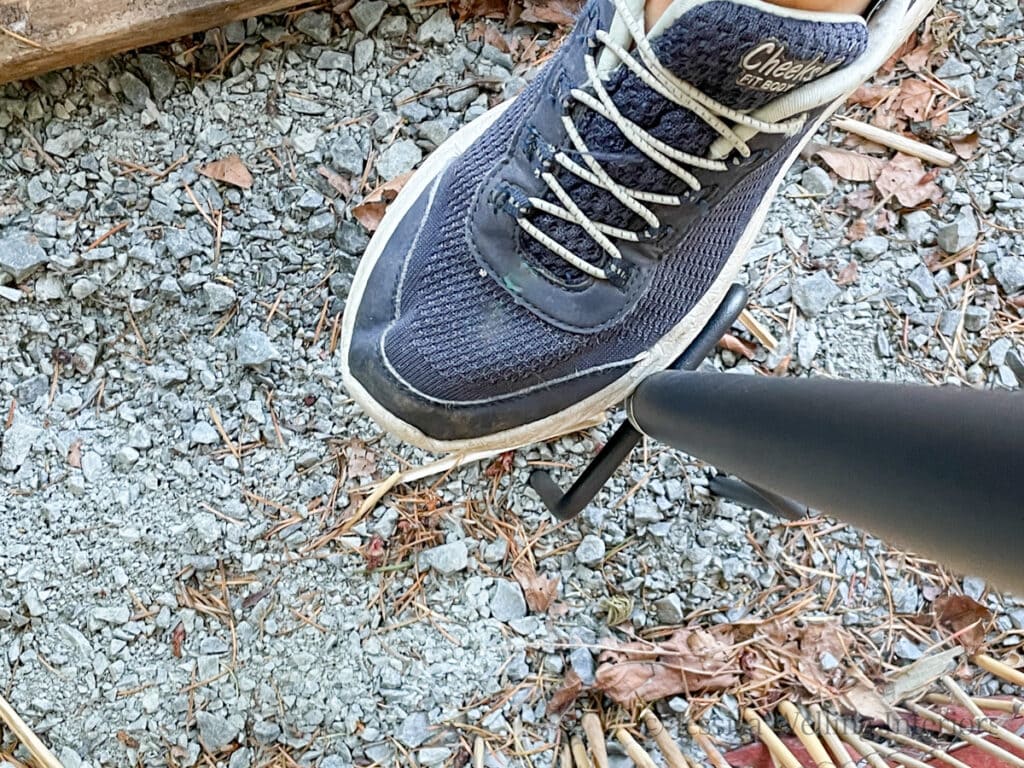 foot standing on the base of a fork-style string light pole to insert it into the ground